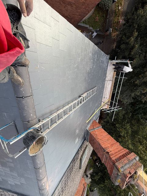 Completed new slate roof seen from the ridge with ladder and chimney
